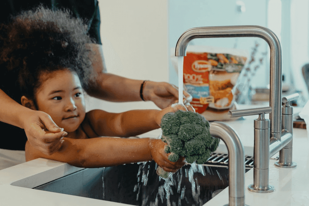 A girl washing broccoli in the kitchen sink